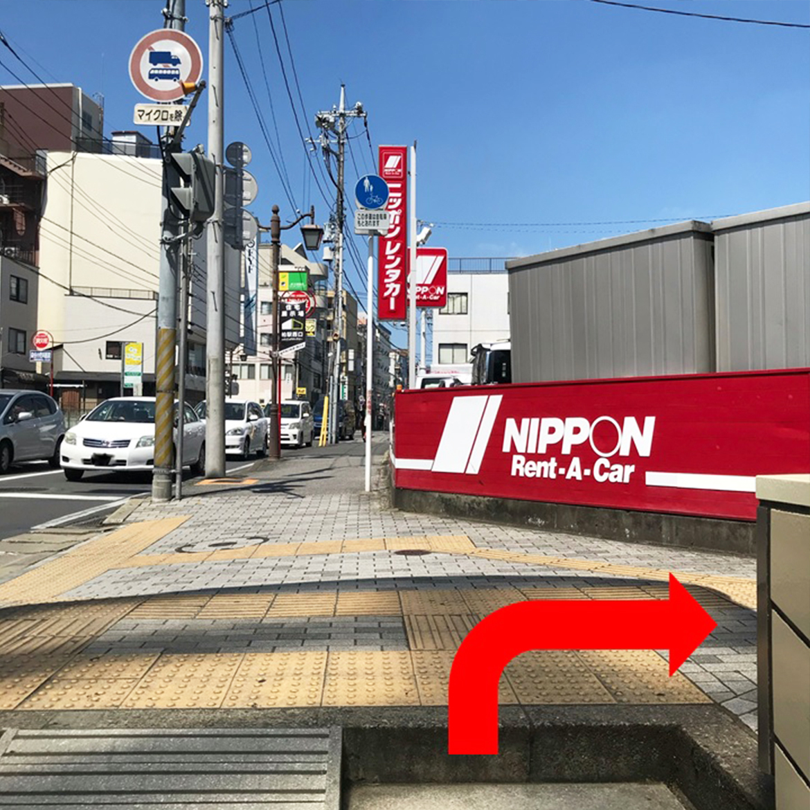 ⑤地下道を出たところです。正面にニッポンレンタカーの赤い看板と壁が見えます。赤い壁に沿って右に進みます。